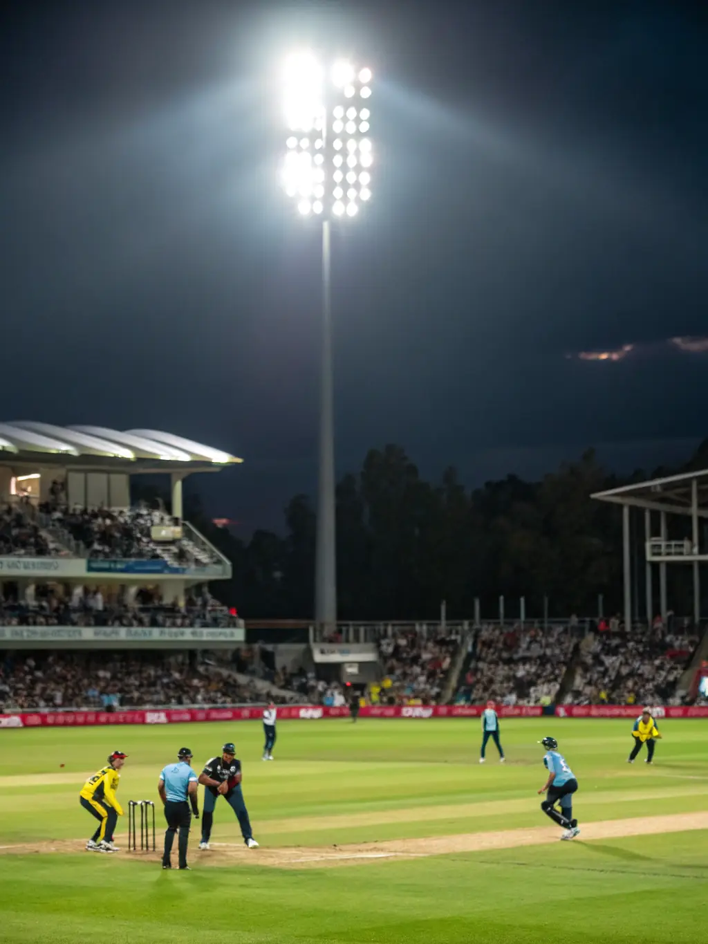A dynamic action shot of a cricket match in progress at Jersey Titans Sportsplex, focusing on the bowler delivering a fast ball during a JTICL game, with fielders in strategic positions and the batsman ready to strike.